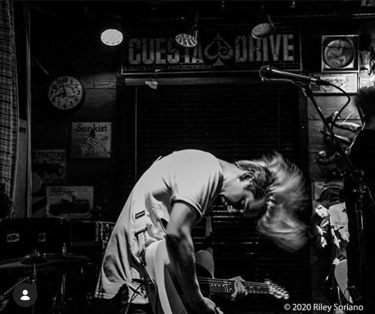 Black and white photograph of a guitarist in motion onstage